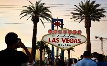 Az emberek fényképeket készítenek a mesés Las Vegas -i panel fogadásával egy ködös narancssárga ég alatt, míg a nap 2023. július 29 -én tart.