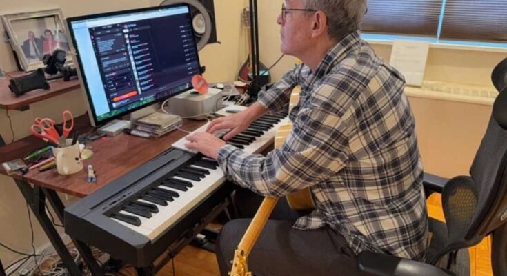 Ebben a képen John Beltzer, a Love Foundation Songs of Love Foundation egy elektronikus zongorabillentyűzeten található, és eltalálja a fenti számítógépes billentyűzetet. Egy számítógépes oktatóra néz, aki a zongora billentyűzet mögött található íróasztalon van. Egy gitár az ölében nyugszik.