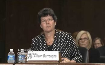 Ebben a képernyőképen az Allison Burroughs egy olyan asztalnál ül, amely mikrofonnal van felszerelve a Szenátus megerősítő közönsége során 2014 -ben, hogy amerikai kerületi bíróvá váljon.