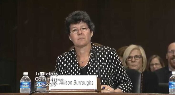 Ebben a képernyőképen az Allison Burroughs egy olyan asztalnál ül, amely mikrofonnal van felszerelve a Szenátus megerősítő közönsége során 2014 -ben, hogy amerikai kerületi bíróvá váljon.